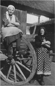 Eine alte Frau trägt noch eine der typischen Blaudruckschürzen. Diese bessere Schürze ersetzte schnell die Alltagsschürze, etwa dann, wenn man fotografiert wurde. Beide Frauen tragen Holzpantinen, das bis in die 50er Jahre übliche Alltagsschuhwerk.